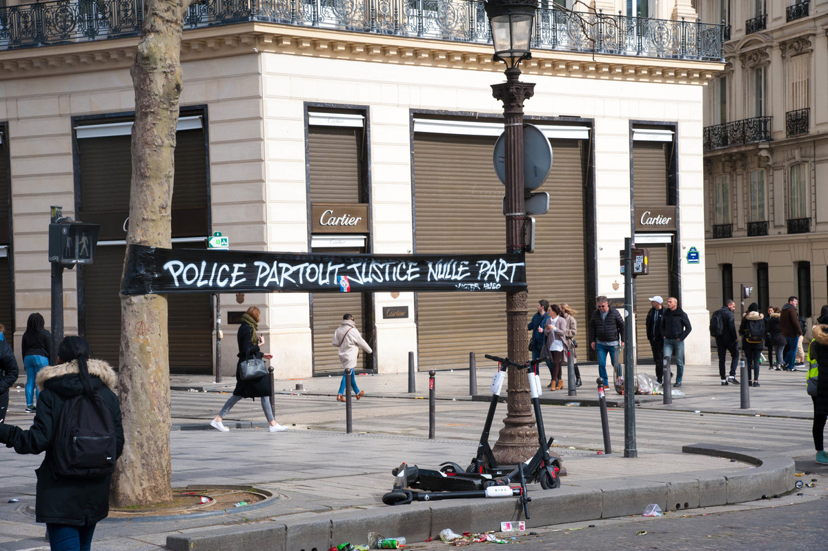 Sur les Champs-Élysées, des tags éphémères écrits sur du plastic tendu entre deux arbres - © Reflets